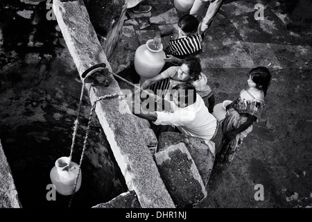 Indische Frauen und Männer ziehen Wasser aus einem Brunnen in einem indischen Dorf Straße. Andhra Pradesh, Indien. Monochrom Stockfoto