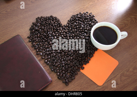Die Kaffeebohnen Bild arrangiert eine Herzform und Papier Notebook mit Orange platziert. Stockfoto