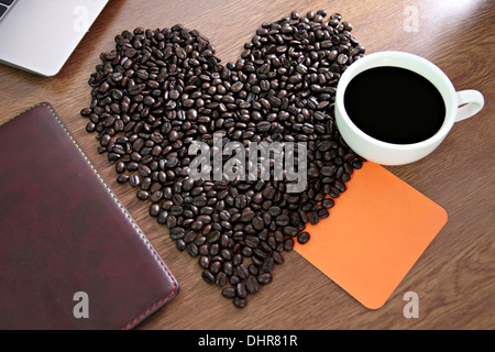 Die Kaffeebohnen Bild arrangiert eine Herzform und Papier Notebook mit Orange platziert. Stockfoto