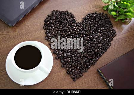 Das Bild der Kaffeebohnen in Form eines Herzens, in der Nähe von Kaffee weiß und grün Pfefferminze angeordnet. Stockfoto