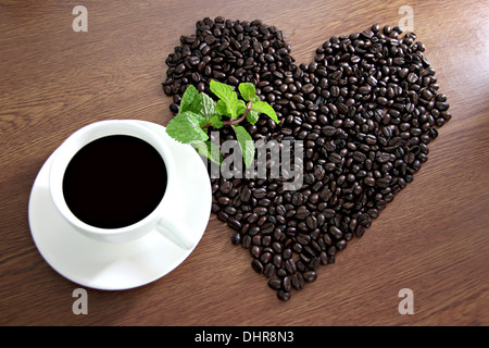 Das Bild der Kaffeebohnen in Form eines Herzens, in der Nähe von Kaffee weiß und grün Pfefferminze angeordnet. Stockfoto