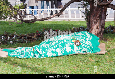 Einsame Obdachlose Person schlafend unter eine alte Decke außerhalb in einem Stadtpark center Stockfoto