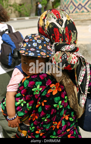 Usbekische Lady in Usbekistan mit einem kleinen Kind. Sie trägt traditionelle Khan-Atlas-Tunika-Kleid mit gestickten Mustern. Stockfoto