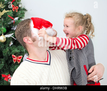 Vater und Tochter auf dem Weihnachtsmarkt Spaß zu haben. Mädchen versuchen, auf Weihnachtsmütze auf Vater legen. Stockfoto