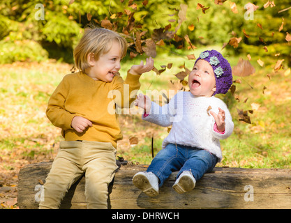 Kinder werfen Blätter im herbstlichen Wald Stockfoto