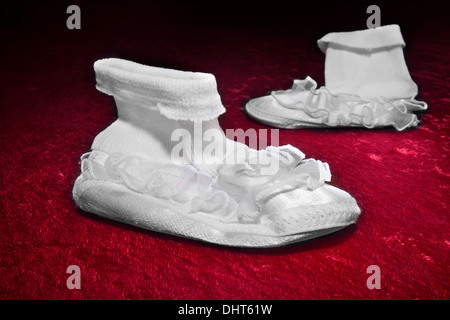 Ein paar der alten baby Hausschuhe auf rot, crushed Velvet. Stockfoto