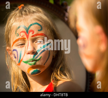 Porträt eines emotionalen kleine Mädchen mit Farbe im Gesicht sieht in den Spiegel. Stockfoto