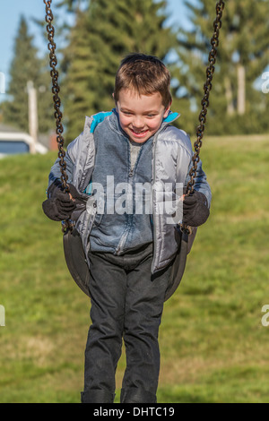 Model freigegeben, niedlich, Lächeln, lachen, 5 Jahre alter Junge, Spaß in der Natur auf der Schaukel. Stockfoto