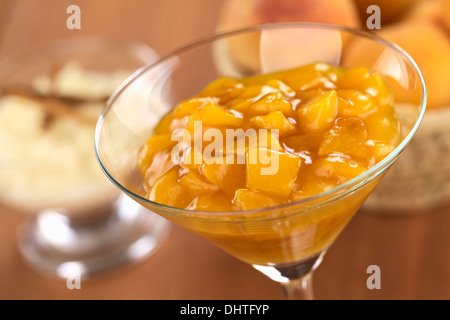 Frischen Pfirsich Kompott im Cocktailglas mit Milchreis und Korb voller Pfirsiche in den Rücken Stockfoto