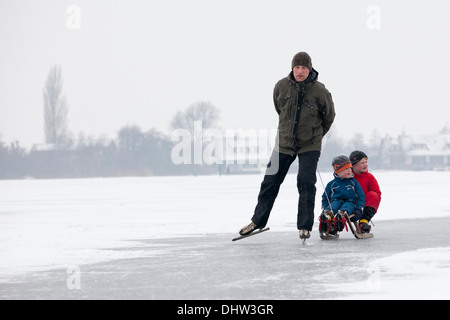 Niederlande, Loosdrecht, Seen genannt Loosdrechtse Plassen. Winter. Vater Eislaufen mit Söhnen auf Schlitten Stockfoto