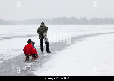 Niederlande, Loosdrecht, Seen genannt Loosdrechtse Plassen. Winter. Vater Eislaufen mit Söhnen auf Schlitten Stockfoto