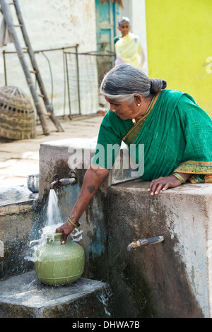 Indische Seniorin einen Kunststoff-Topf mit Wasser aus einem Standrohr in einem ländlichen Dorf zu füllen. Andhra Pradesh, Indien Stockfoto