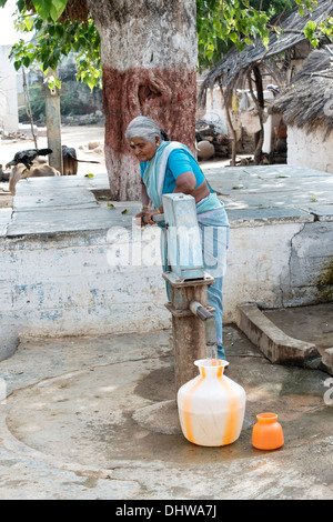 Indische Seniorin Pumpen von Wasser aus einer Hand-Pumpe in einen Topf in einem indischen Dorf Straße. Andhra Pradesh, Indien Stockfoto