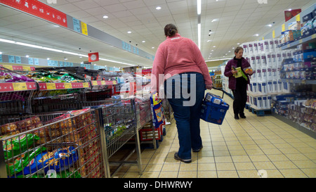 Rückansicht einer übergewichtigen Frau, die in einem Aldi-Laden in Großbritannien IN einem Gang mit Chips (Kartoffelchips) EINKAUFT, KATHY DEWITT Stockfoto