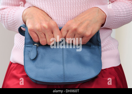 Unsichere ältere Frau sitzt und Fest umklammerte eine Handtasche auf ihrem Schoß mit zwei Händen, die Ihr für die Sicherheit. England, Großbritannien, Großbritannien Stockfoto