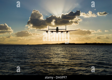 Avro Lancaster Bomber in der Silhouette, Überschrift in den Sonnenuntergang auf niedrigem Niveau über einen Küsten Seestück. Stockfoto
