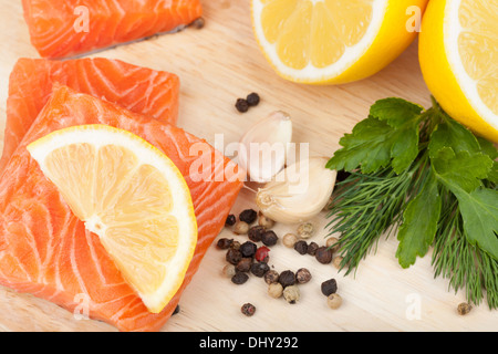 Lachs auf Schneidebrett mit Zitronen und Kräutern. Closeup Stockfoto