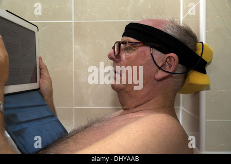 Ältere Mann liest iPad in der Badewanne, den Kopf auf eine behelfsmäßige Kopfstütze ruht Stockfoto