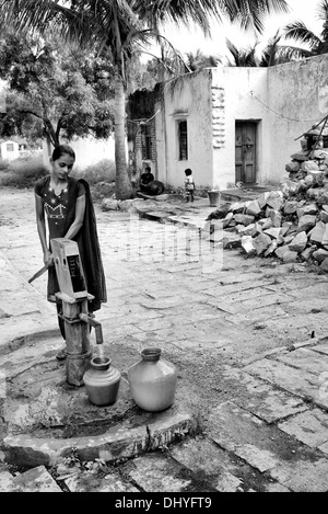 Indische Teenager-Mädchen Pumpen von Wasser aus einer Hand-Pumpe in einen Topf in einem indischen Dorf. Andhra Pradesh, Indien. Monochrom Stockfoto