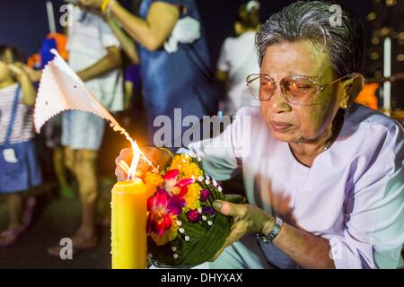 Bangkok, Thailand. 17. November 2013. Eine Frau zündet die Kerze auf ihre Krathong vor in den Chao Phraya River in der Nähe von Wat Yannawa in Bangkok zu schweben. Loy Krathong (auch geschrieben als Loi Krathong) wird jährlich in ganz Thailand und bestimmte Teile von Laos und Burma (im Shan-Staat) gefeiert. Der Name könnte übersetzt '' schwebende Krone '' oder '' schwimmende Dekoration '' und stammt aus der Tradition in der Herstellung von heiter Dekorationen, die dann auf einem Fluss geschwommen sind. Stockfoto