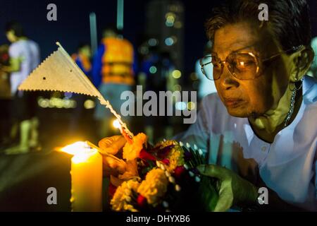 Bangkok, Thailand. 17. November 2013. Eine Frau zündet die Kerze auf ihre Krathong vor in den Chao Phraya River in der Nähe von Wat Yannawa in Bangkok zu schweben. Loy Krathong (auch geschrieben als Loi Krathong) wird jährlich in ganz Thailand und bestimmte Teile von Laos und Burma (im Shan-Staat) gefeiert. Der Name könnte übersetzt '' schwebende Krone '' oder '' schwimmende Dekoration '' und stammt aus der Tradition in der Herstellung von heiter Dekorationen, die dann auf einem Fluss geschwommen sind. Stockfoto