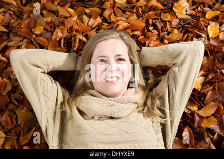 Horizontale Foto eine glückliche Erwachsene Reife Frau liegend auf einem Bett aus Herbst Blätter Stockfoto