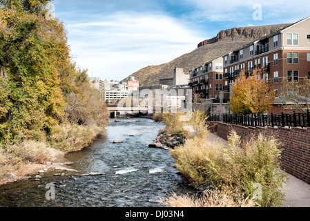 GOLDEN, Colorado - Clear Creek in Golden, Colorado, führt zur Coors Brewery, die in der Ferne zu sehen ist, wobei ein Teil des Tafelbergs im Hintergrund rechts zu sehen ist. Das Golden Today wurde während des Pike's Peak Gold Rush gegründet und ist bekannt für sein reiches Erbe, Outdoor-Aktivitäten und den Geburtsort der Coors Brewery, die eine einzigartige Mischung aus Geschichte, Kultur und natürlicher Schönheit verkörpert. Stockfoto