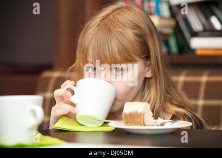 Kleines blondes Mädchen trinkt Tee mit Kuchen Stockfoto