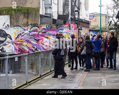 Eine Gruppe von Touristen, die Teilnahme an einer Tour von street Art und Graffiti im East End von London Stockfoto