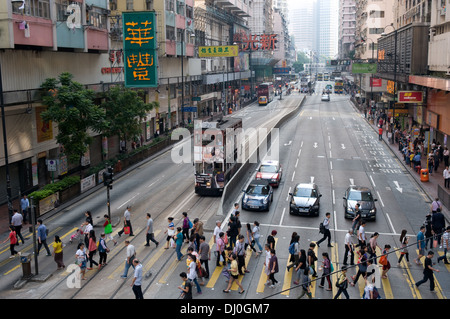 Eine Straßenbahn und Verkehr warten, während Fußgänger Königsweg im North Point von Hong Kong Island überquert. Stockfoto