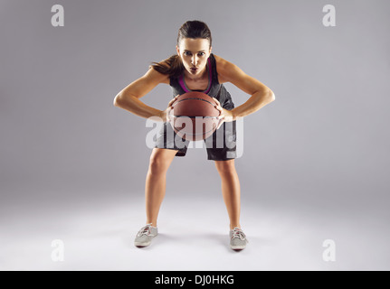 In voller Länge Portrait von weiblichen Basketball-Spieler den Ball auf grauem Hintergrund. Schöne Frau in Sportbekleidung Stockfoto