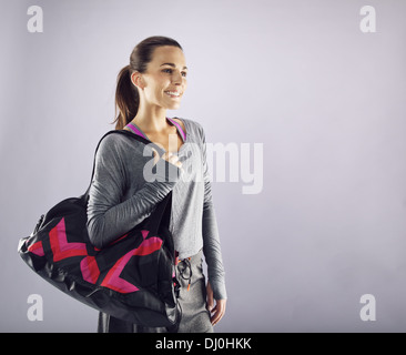 Bild der schönen kaukasischen Sportlerin mit dem Fitnessstudio Tasche schauen weg Lächeln auf den Lippen. Junge Frau in Sportkleidung tragen Sporttasche Stockfoto