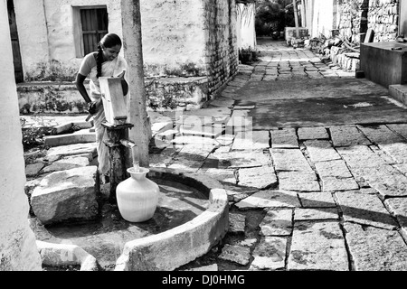 Indische Frau Füllung Kunststoff Wassertopf aus einem ländlichen Dorf Handpumpe. Andhra Pradesh, Indien. Monochrom Stockfoto