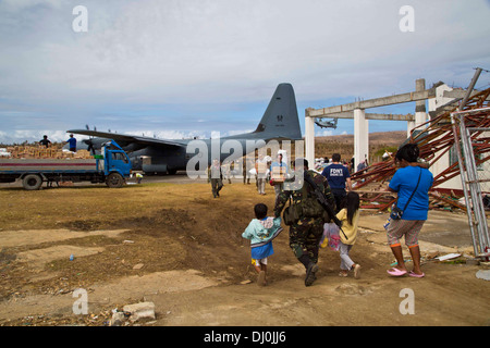 GUIUAN, Republik der Philippinen (17. November 2013) ein Mitglied der Streitkräfte der Philippinen führt eine Familie, ein Royal Australian Air Force c-130 zu Guiuan Flughafen, Republik der Philippinen während Betrieb Damayan, 17 November geflogen werden. Th Stockfoto