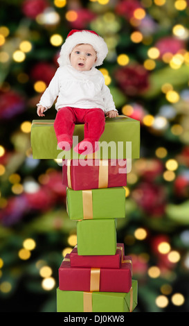 Santa Baby mit Weihnachtsmütze sitzt auf einem großen Stapel von Geschenken Stockfoto