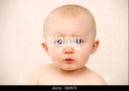 Blue eyed Baby Junge schaut in die Kamera, schmollend auf einem weichen Pfirsich farbigen Hintergrund Stockfoto