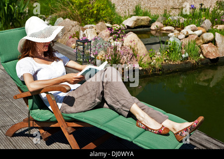 Frau liest am Teich, entspannen Sie sich auf eine Wiese im Garten, im Hintergrund einen schöneren Steingarten Stockfoto