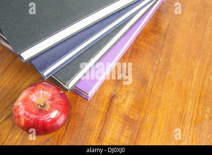 roter Apfel und alte Bücher auf hölzernen Tischplatte Stockfoto