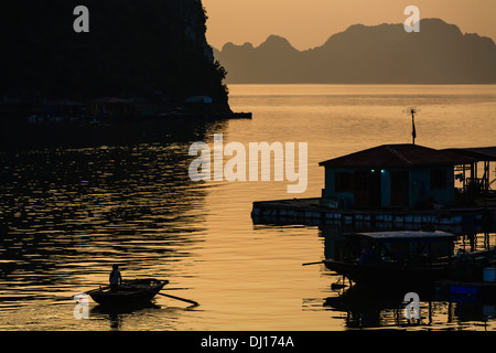 Silhouette Abbildung Ruderboot zwischen den schwimmenden Dörfern auf Halong-Bucht in Vietnam bei Sonnenuntergang Stockfoto