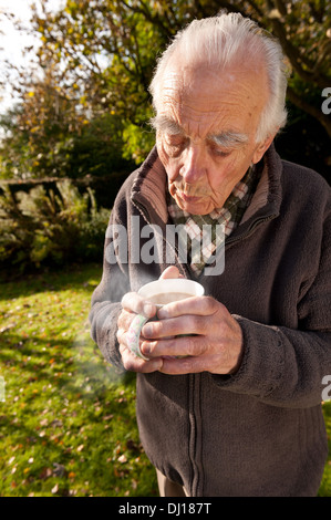 Kalte Hände mit einer dampfenden Tasse Tee aufwärmen, nach Gartenarbeit an kalten sonnigen Herbsttag Stockfoto