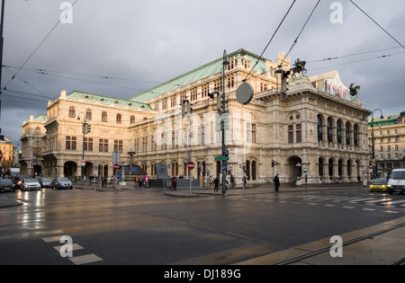 Wiener Staatsoper und der Wiener Ringstraße bei Sonnenuntergang. Eine feuchten Straße unterstreicht das massive Gebäude aus Steine. Stockfoto