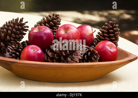 Rote Äpfel und Tannenzapfen in einer Holzschale Stockfoto
