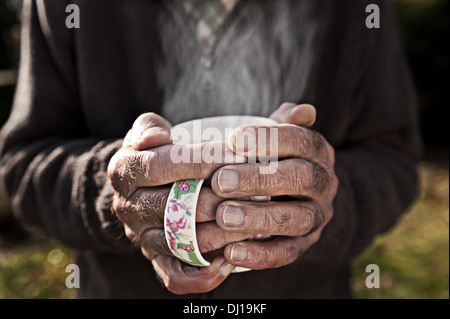 Kalte Hände mit einer dampfenden Tasse Tee aufwärmen, nach Gartenarbeit an kalten sonnigen Herbsttag Stockfoto