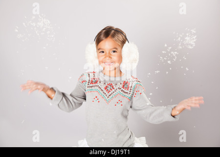 Kleines Mädchen trägt Ohrenschützer und wirft Schnee in der Luft Stockfoto