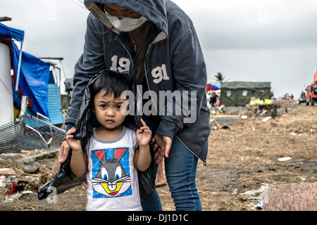 Eine philippinische Mutter Vorhänge ihres Sohnes mit einer Plastiktüte, ihn vor dem Regen zu schützen, während des Wartens auf Hilfsgüter in der Nachmahd des Super Taifun Haiyan 17. November 2013 in Tacloban, Philippinen erhalten. Stockfoto