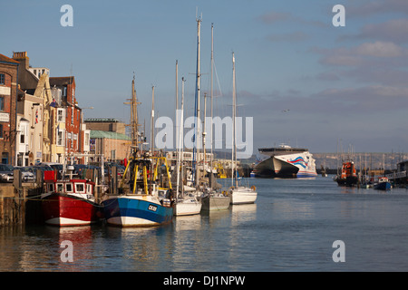 Am Hafen von Weymouth, Weymouth Quay, liegen Boote vor, die im November in Weymouth, Dorset, in der Ferne mit der Condor Express-Fähre anlegt Stockfoto