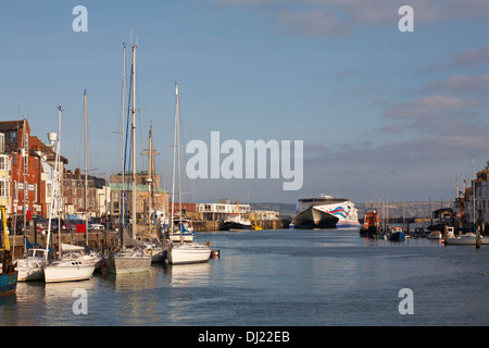 Am Hafen von Weymouth, Weymouth Quay, liegen Boote vor, die im November in Weymouth, Dorset, in der Ferne mit der Condor Express-Fähre anlegt Stockfoto