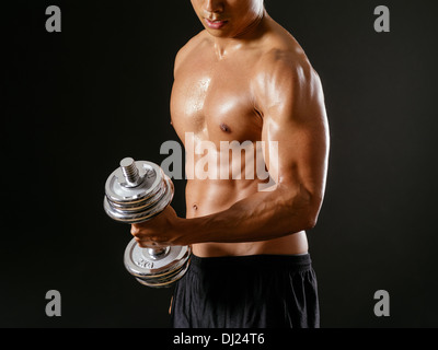 Foto von einem asiatischen Mann mit Hanteln trainieren und dabei Bizeps curls auf dunklem Hintergrund. Stockfoto
