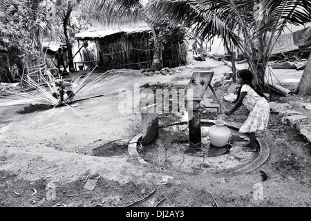 Indische Mädchen Füllung Kunststoff Wassertopf aus einem ländlichen Dorf Handpumpe. Andhra Pradesh, Indien. Schwarz und weiß. Stockfoto