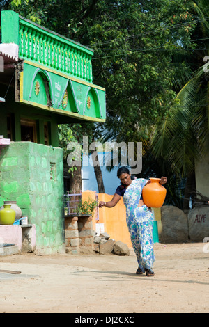 Indische Frau, die einen Kunststoff-Topf mit Wasser aus einer Hand-Pumpe in einem indischen Dorf. Andhra Pradesh, Indien Stockfoto